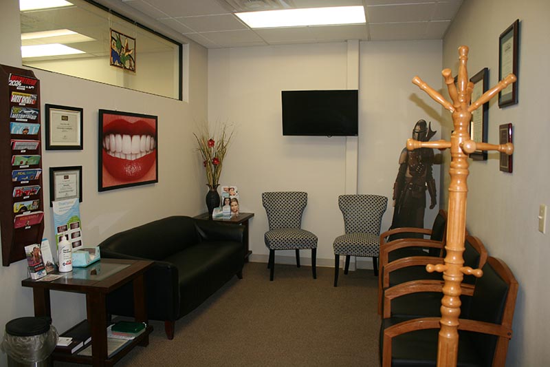 A well-lit dental office waiting room with a comfortable seating area featuring a couch, chairs, and a television.
