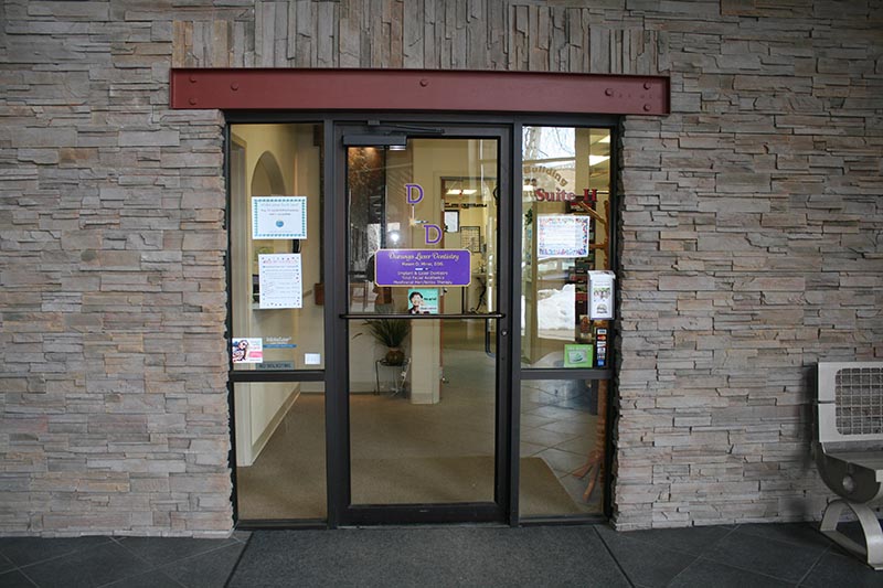 The image shows a building entrance with a brick facade, a glass door, and a sign above the door indicating  Parking Lot.