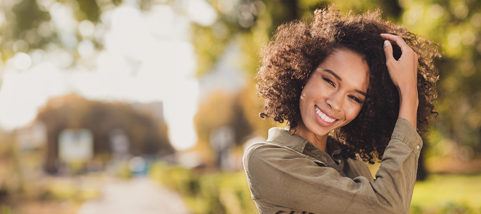 A young woman with curly hair smiling at the camera while standing outdoors.