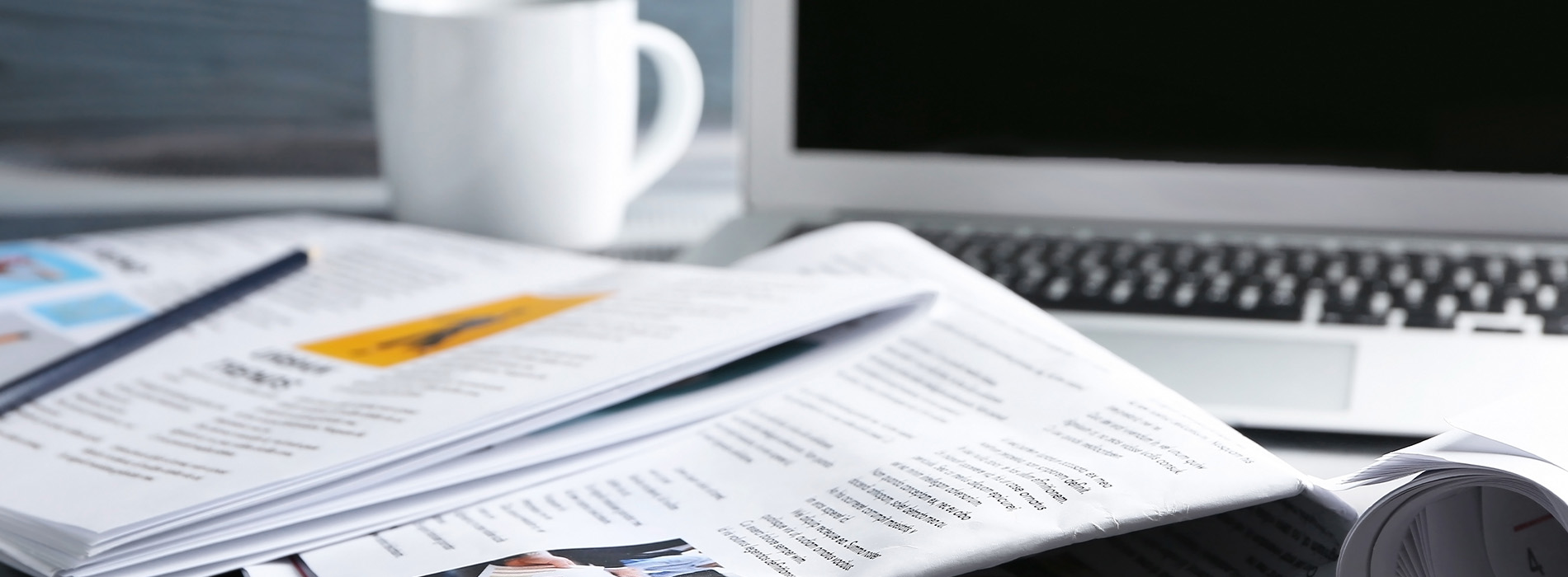 The image depicts a workspace with various papers and documents spread out on a desk, with a laptop and keyboard visible, along with a coffee cup and a smartphone.