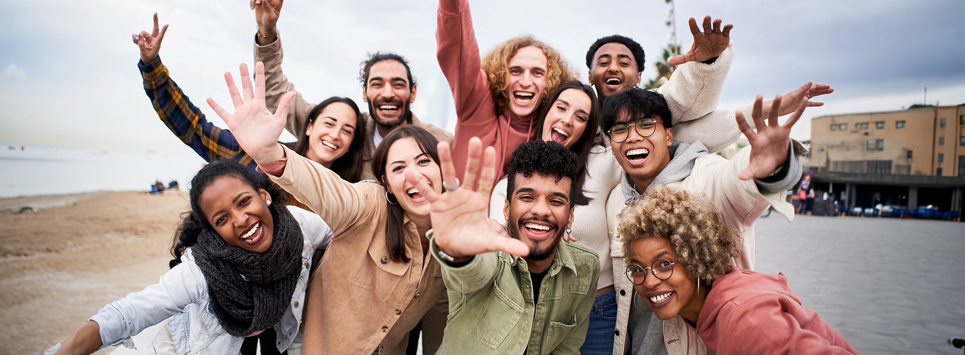 This is a photograph of a group of people posing together with their arms raised, smiling and looking towards the camera, standing outdoors during the day.