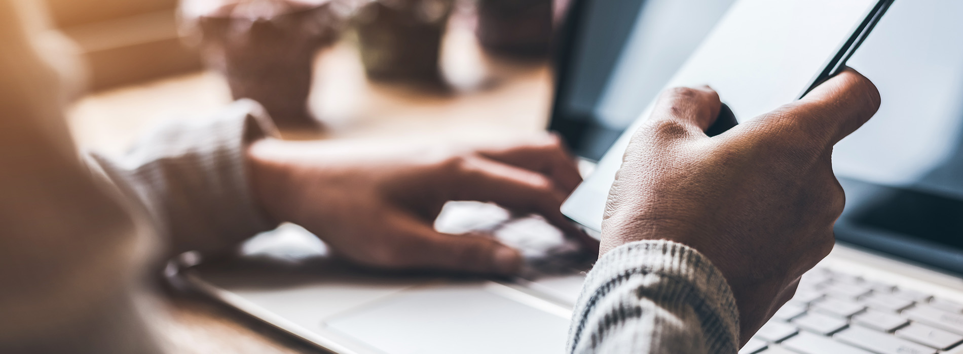 The image depicts a blurred scene with a person using a laptop at a table, surrounded by various items like a cup, a mouse, and a keyboard.