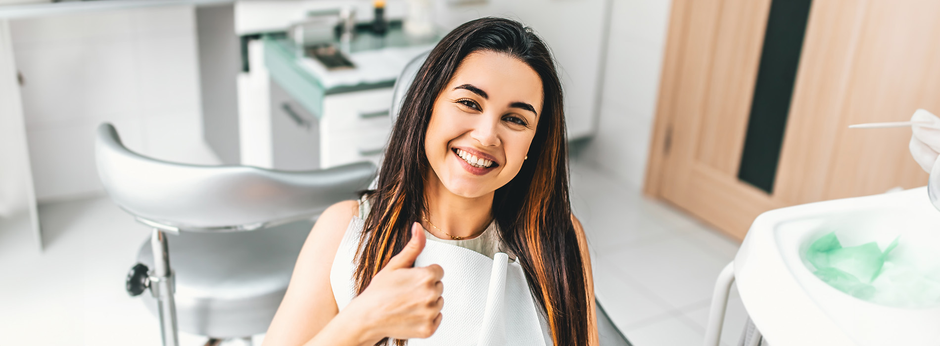 A woman with long dark hair smiling at the camera while standing in a bathroom.