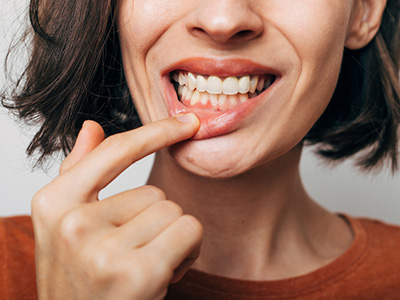 A woman with her finger in her mouth, looking downward.