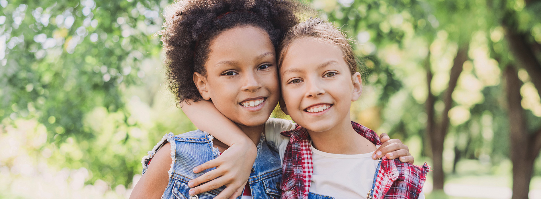 The image shows two children hugging each other outdoors with trees in the background.