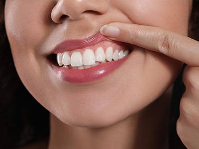 The image shows a woman with teeth brushing her teeth while another person holds up a finger, both set against a blurred background.