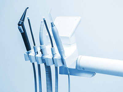 The image shows a collection of medical equipment, including a dental drill, with various tubes and attachments, mounted on a wall, likely in a dental office setting.