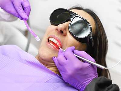 A woman receiving dental care with purple gloves and equipment on her face.