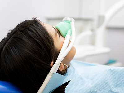The image shows a person lying on a dental chair with their head secured by straps, wearing an oxygen mask, and hooked up to medical equipment.