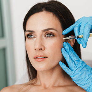 The image shows a woman receiving cosmetic treatment, with a focus on her face being treated with a device held by someone wearing medical gloves.