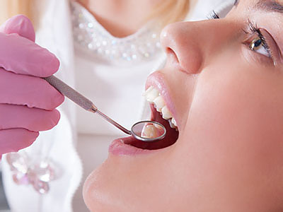 Woman receiving dental treatment with a dentist using dental tools, both wearing gloves and masks for safety.