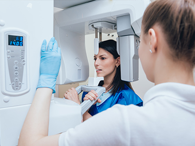 The image shows two individuals standing in front of a large medical imaging machine, with one person operating the machine while another observes.