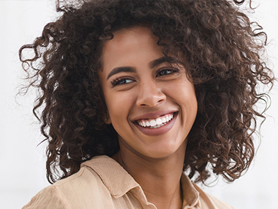 The image features a smiling woman with curly hair, wearing a light-colored top, against a blurred background.
